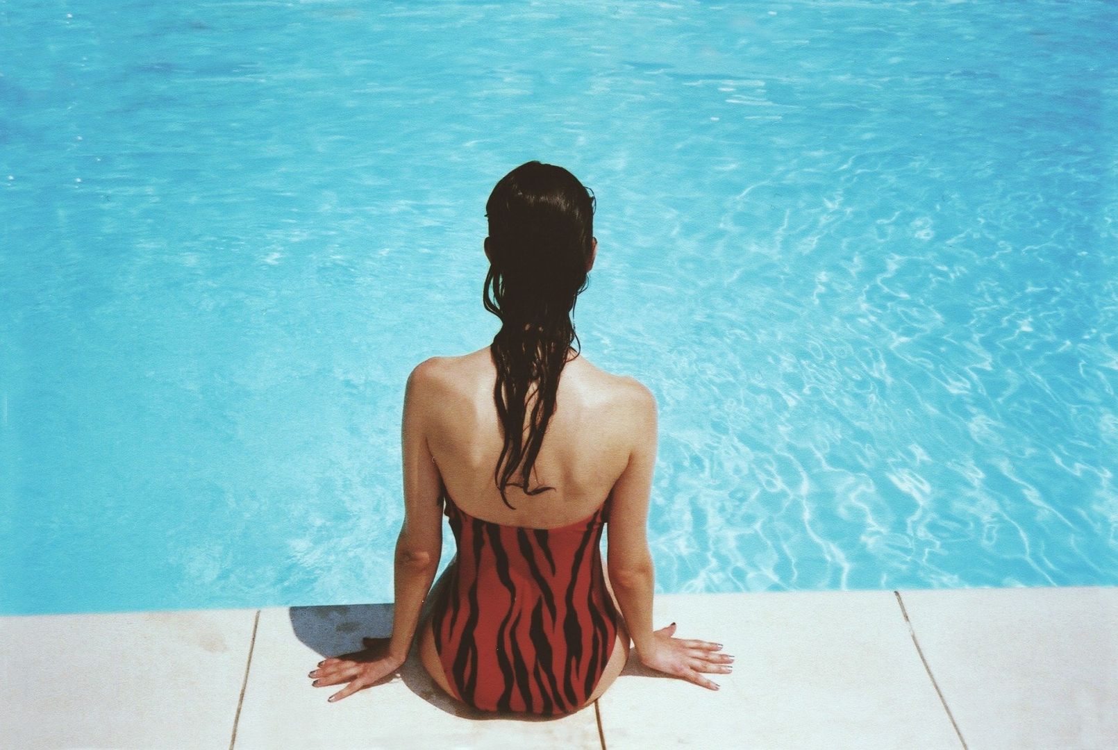 Красивая женщина перед бассейном снимает легкий купальник